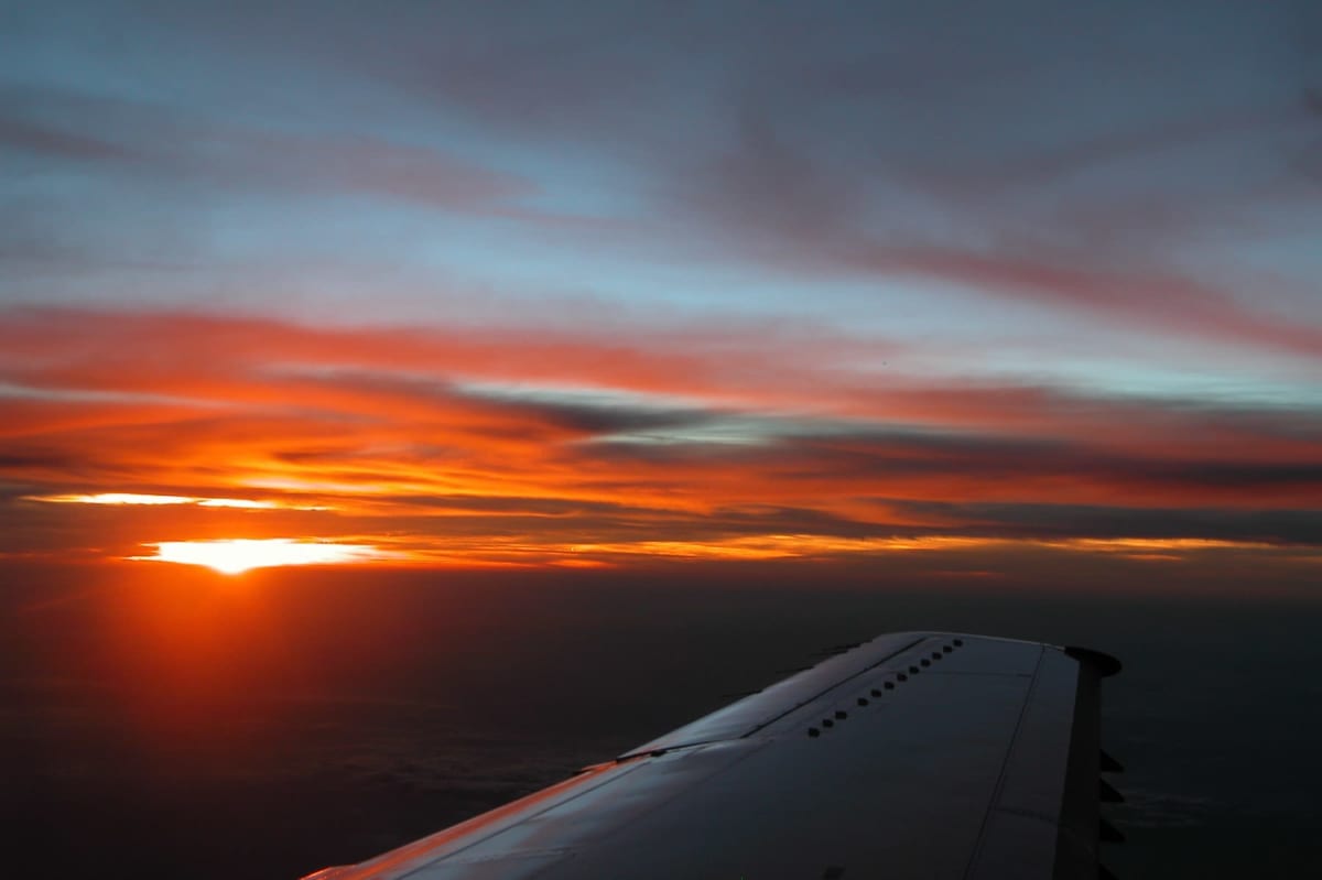 A burning orange sunset along the horizon seen over an aircraft wing at altitude